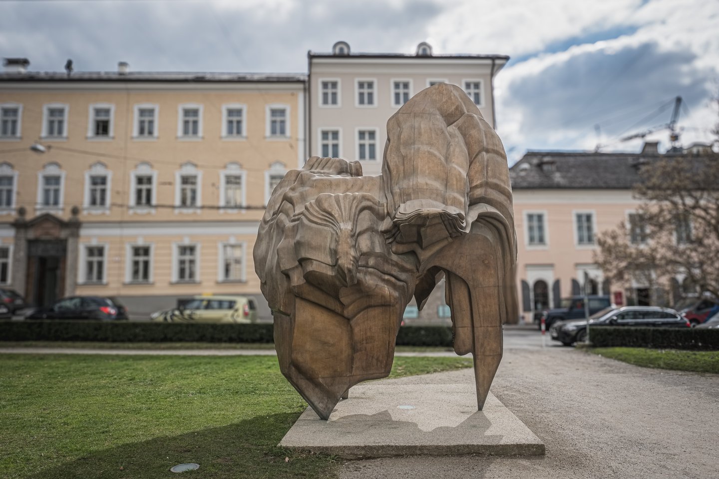 Caldera seen from behind on Makartplatz, its heavy bronze folds turning away from the camera in front of the yellow and pale pink town houses that line the square.