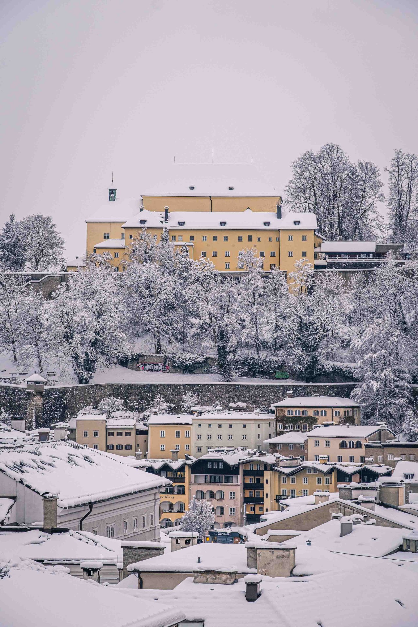 Capuchin Monastery on the Kapuzinerberg with yellow facade in fresh snow viewed from the Salzburg old town below