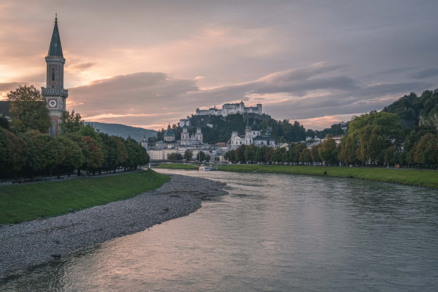 Christuskirche spire rising beside the Salzach river with Hohensalzburg fortress in the distance at sunrise in Salzburg