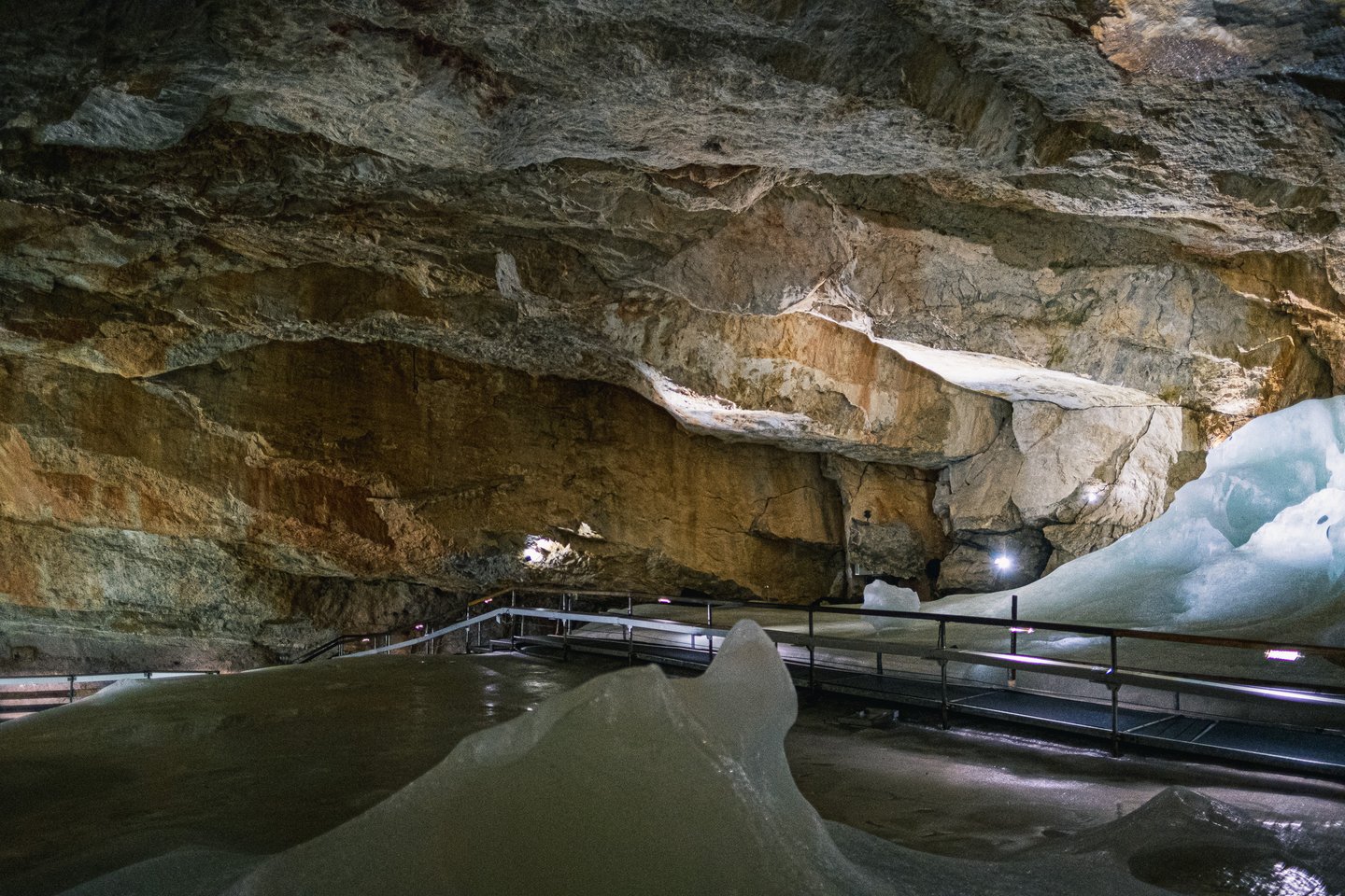 The banded, vaulted rock ceiling of the Dachstein Giant Ice Cave arches over a smooth ice floor, with the lit walkway running along the right-hand wall.