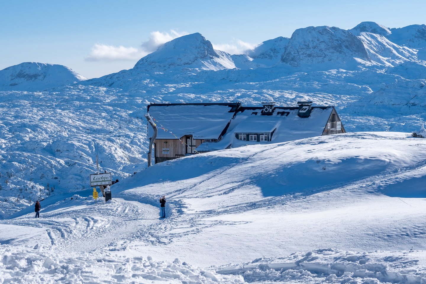 The Lodge am Krippenstein sits half buried in deep snow on the Dachstein plateau, its roof loaded white, with the snow-covered massif rising behind.