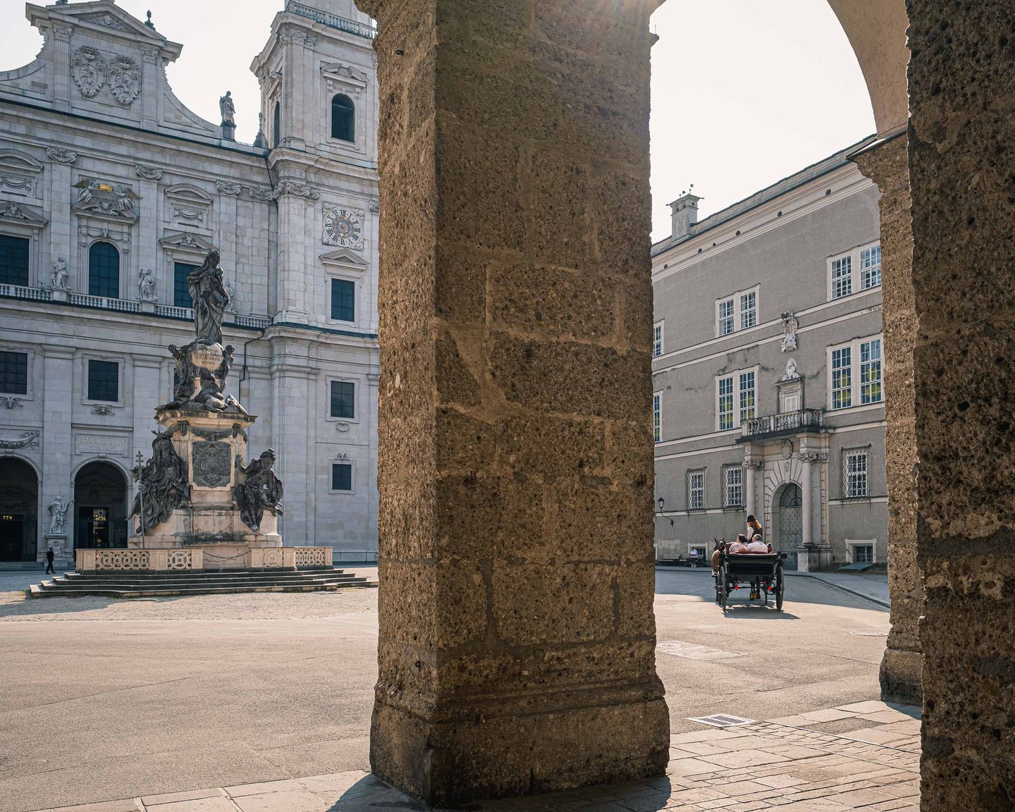 Mariensaule on Domplatz framed by stone arcade pillar with fiaker in Salzburg old town