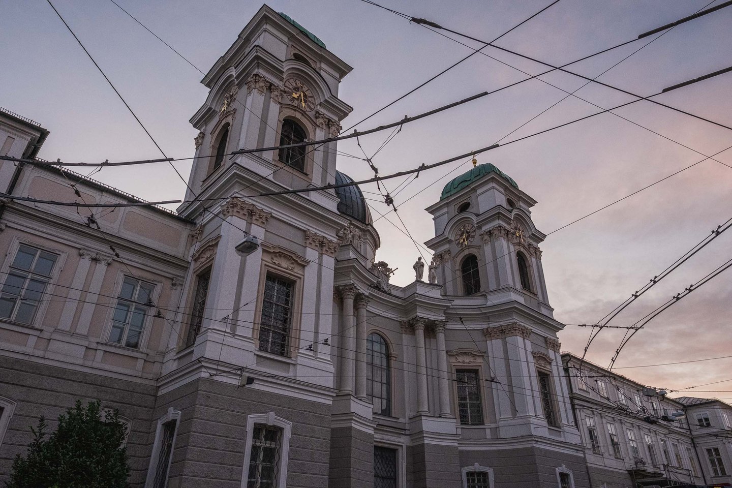 Dreifaltigkeitskirche twin-tower baroque facade at dawn with tram wires crossing the sky in Salzburg.