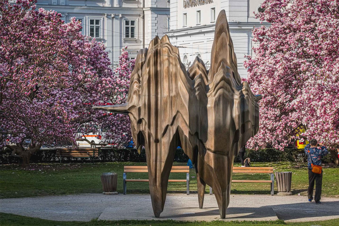 Bronze sculpture with upward flames surrounded by magnolia blossoms near Dreifaltigkeitskirche in Salzburg.