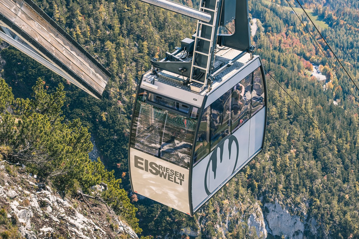 A gondola of the Eisriesenwelt cable car, lettered EIS RIESEN WELT with the ice-stalactite logo, hangs above autumn-coloured forest on the slope near Werfen.