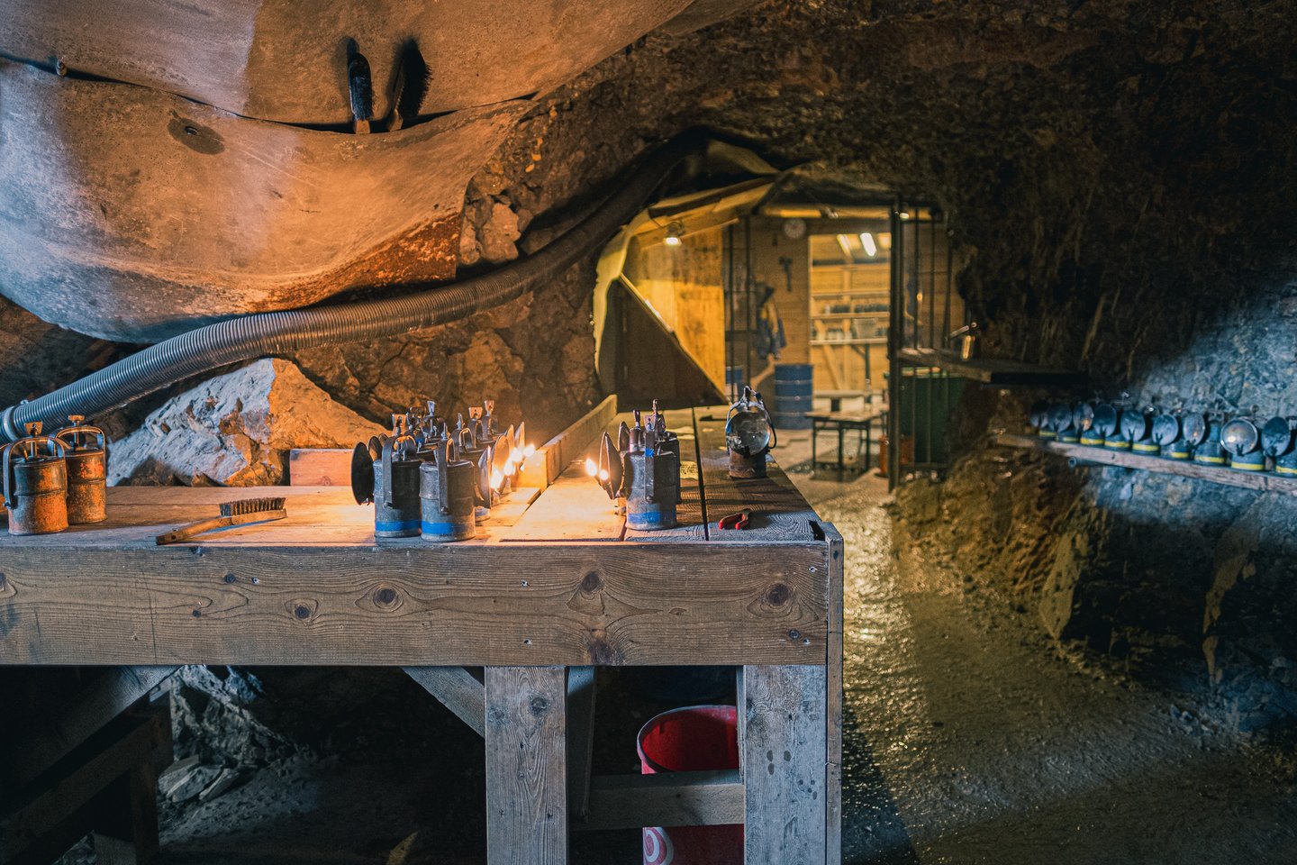 A long wooden bench of carbide lamps burning inside the rock tunnel at the Eisriesenwelt cave entrance, with the lamp store lit up behind it.