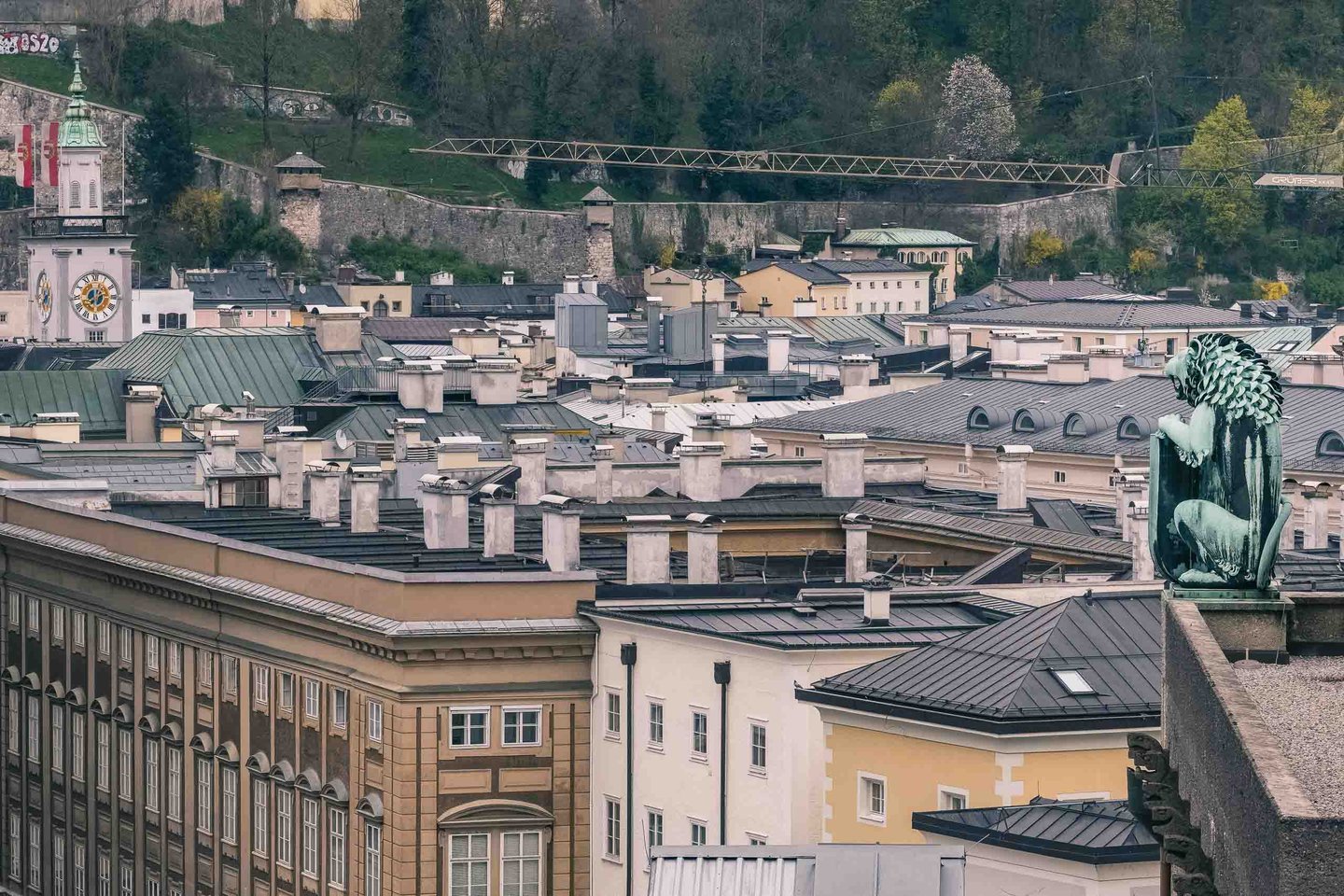 Stone lion sculpture on roof of Festspielhaus overlooks old town rooftops in Salzburg.