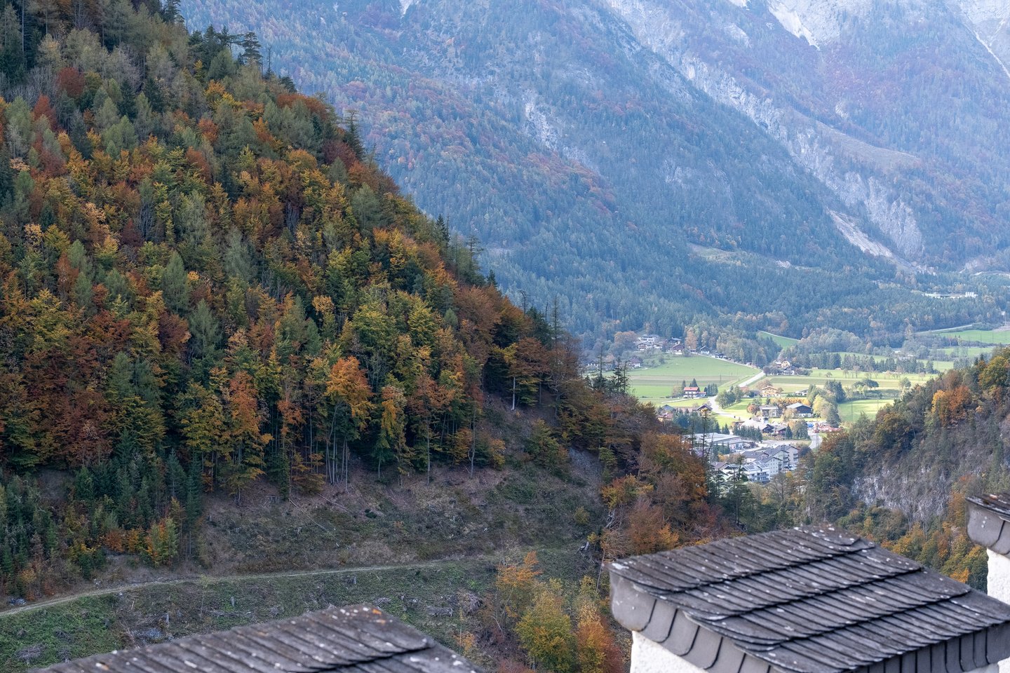 From Festung Hohenwerfen the view drops over shingled roofs and a spur of rust and green autumn forest to the Salzach valley floor with its meadows and scattered houses.