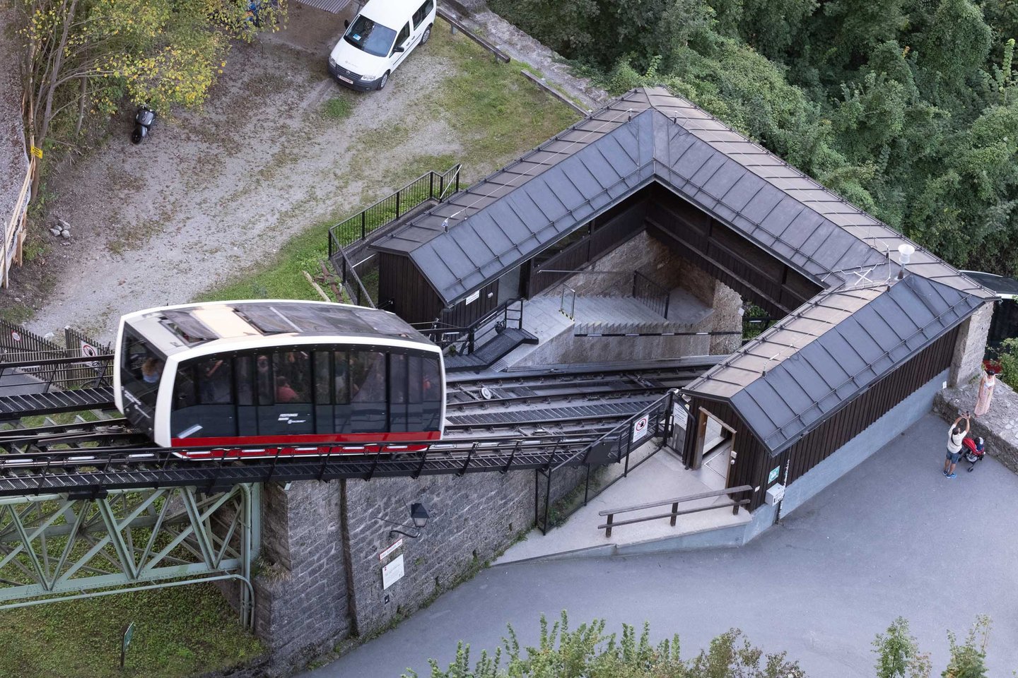 Red and white Festungsbahn funicular cabin descends toward the lower station beside the fortress wall in Salzburg
