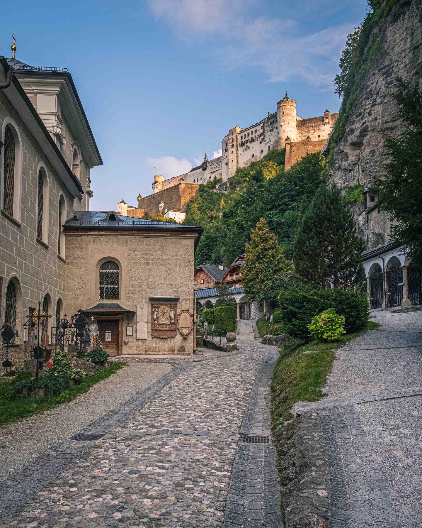 Cobblestone Festungsgasse rising past Petersfriedhof buildings toward Hohensalzburg Fortress in Salzburg old town