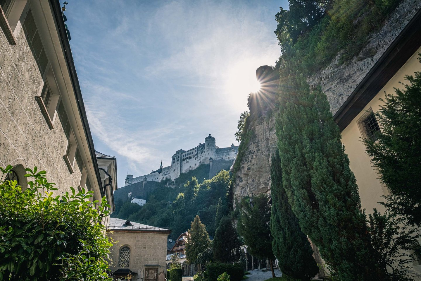 Cobbled Festungsgasse lane rises under the Moenchsberg cliff toward Hohensalzburg Fortress in Salzburg.