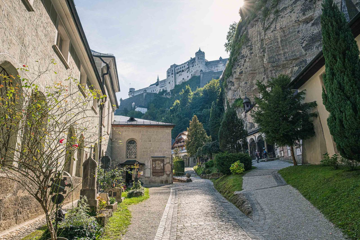Festungsgasse with roadside shrine climbs toward Hohensalzburg Fortress under the Moenchsberg cliff in Salzburg.