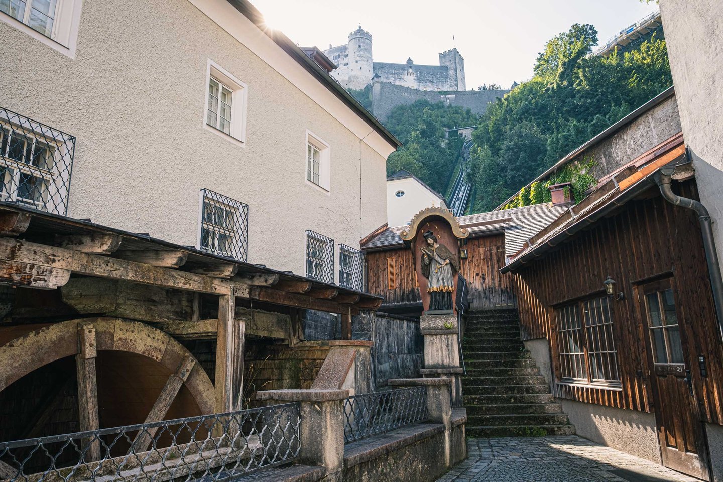 Wooden waterwheel and religious niche on a cobbled lane leading up to Hohensalzburg Fortress in Salzburg.