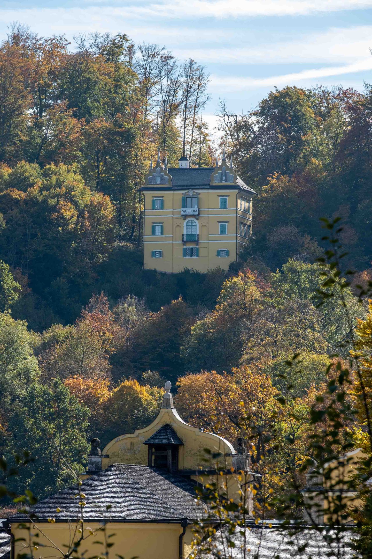 Yellow Monatsschlossl housing the Folklore Museum rising above autumn forest in Hellbrunn