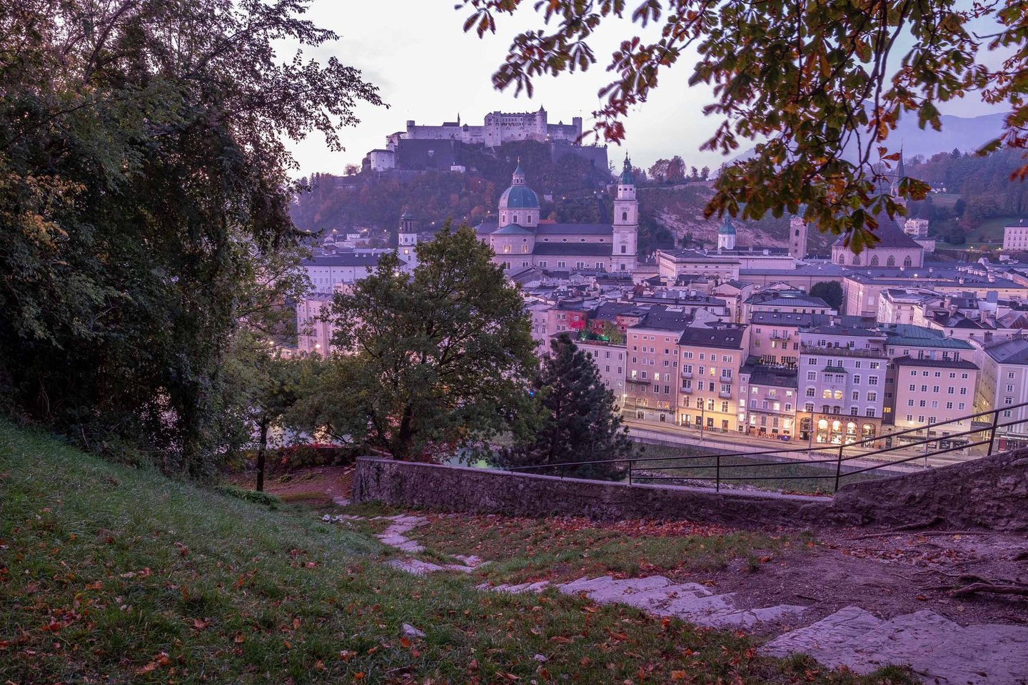 Hohensalzburg fortress and Altstadt rooftops at dawn seen through trees from Kapuzinerberg