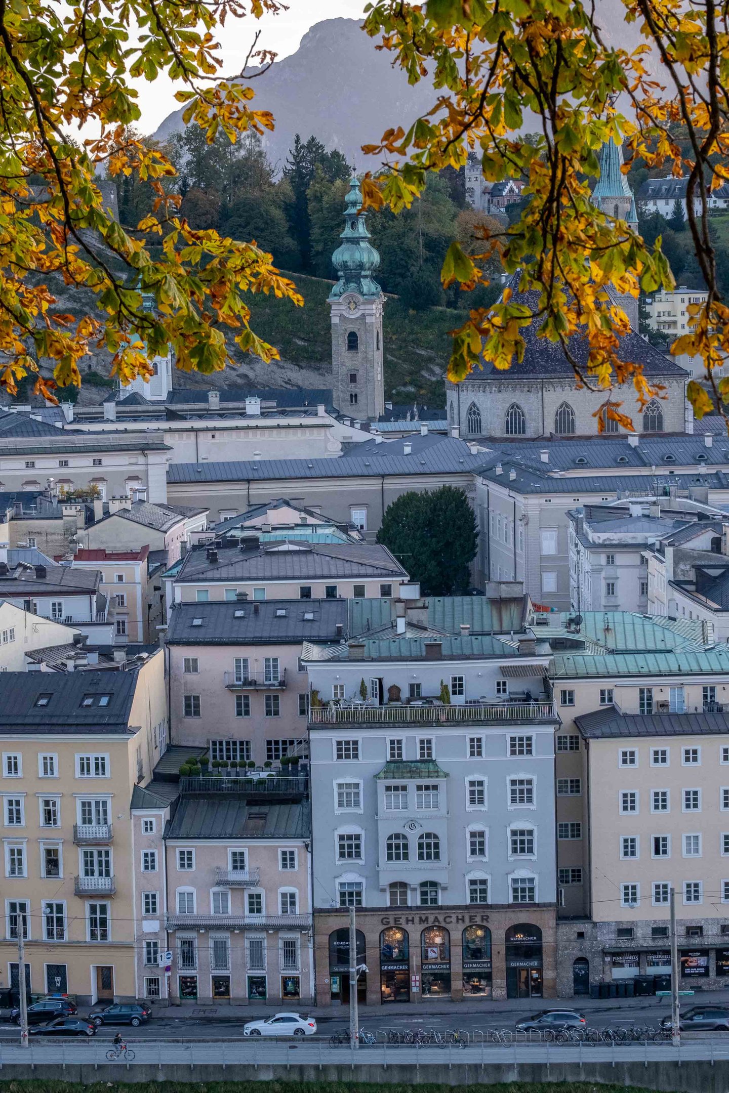 Franziskanerkirche and Rathausturm framed by autumn leaves seen from Kapuzinerberg in Salzburg.