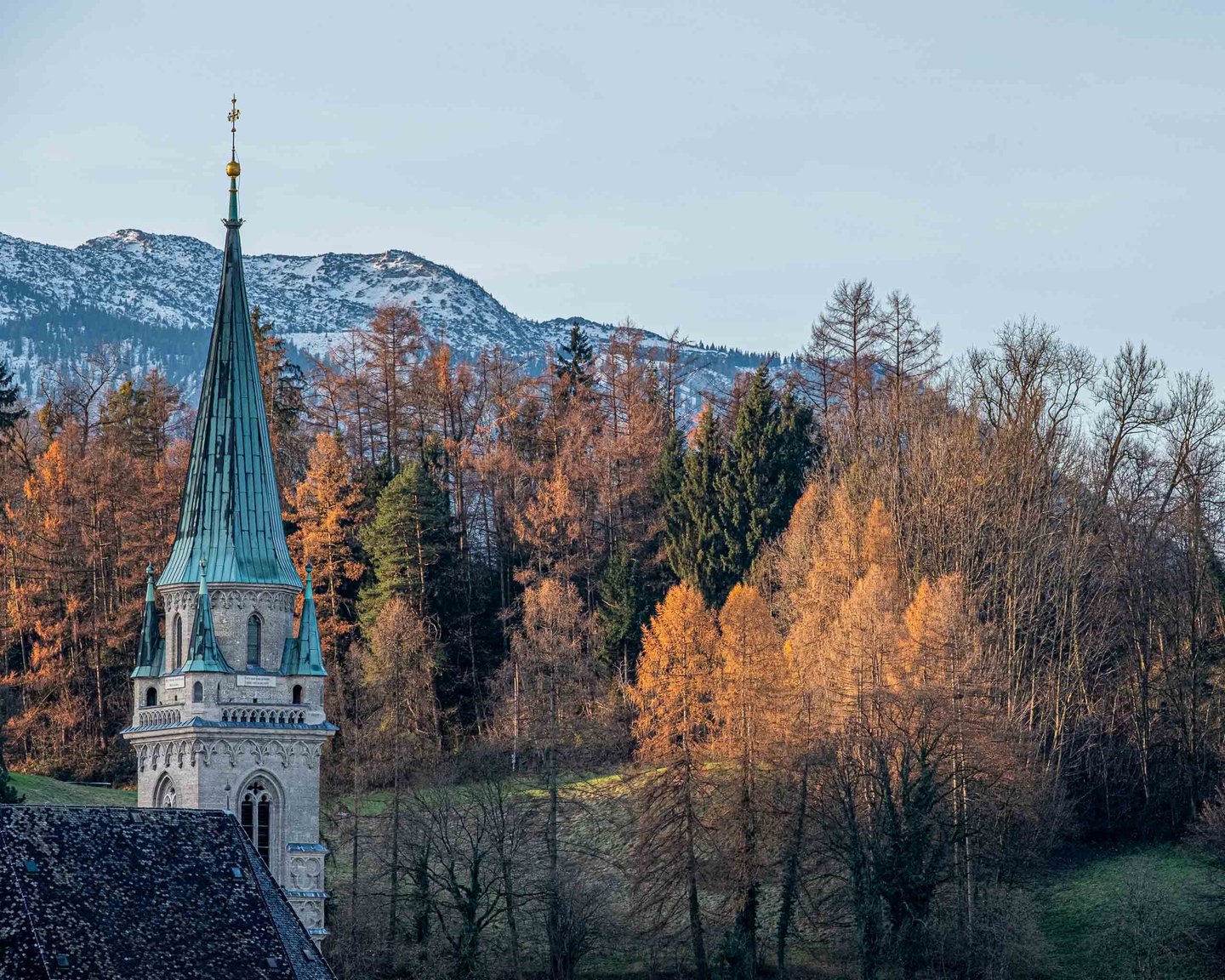 The Franziskanerkirche spire against autumn larches, with the first snow on the ridge behind