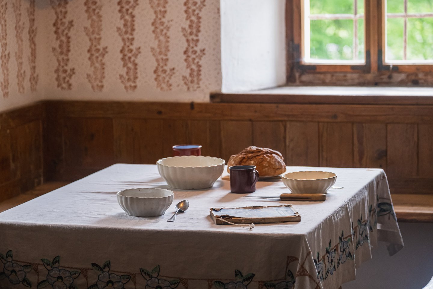 Rustic table set with ceramic bowls bread and mug by a window in a historic farmhouse at the open-air museum near Salzburg.