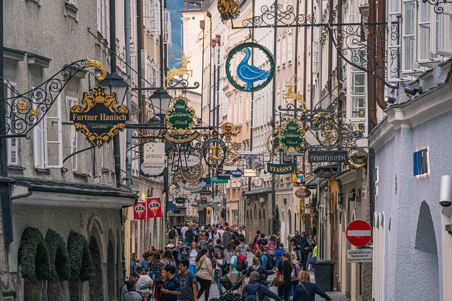Crowded Getreidegasse lined with gilded wrought iron shop signs in Salzburg old town