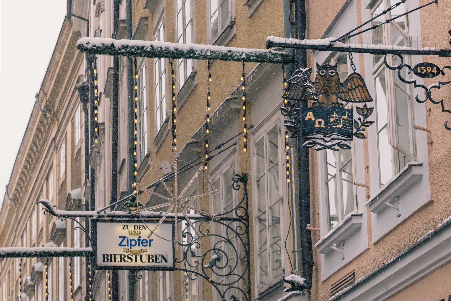 Wrought-iron guild signs of Zipfer Bierstuben hang over Getreidegasse in snowy Salzburg.