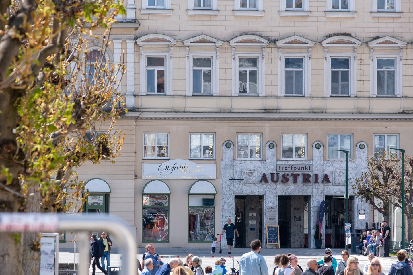 A cream-coloured town house on Gmunden's main square, its ground floor faced in marble under a treffpunkt Austria sign, with people crossing the square in spring sunshine.