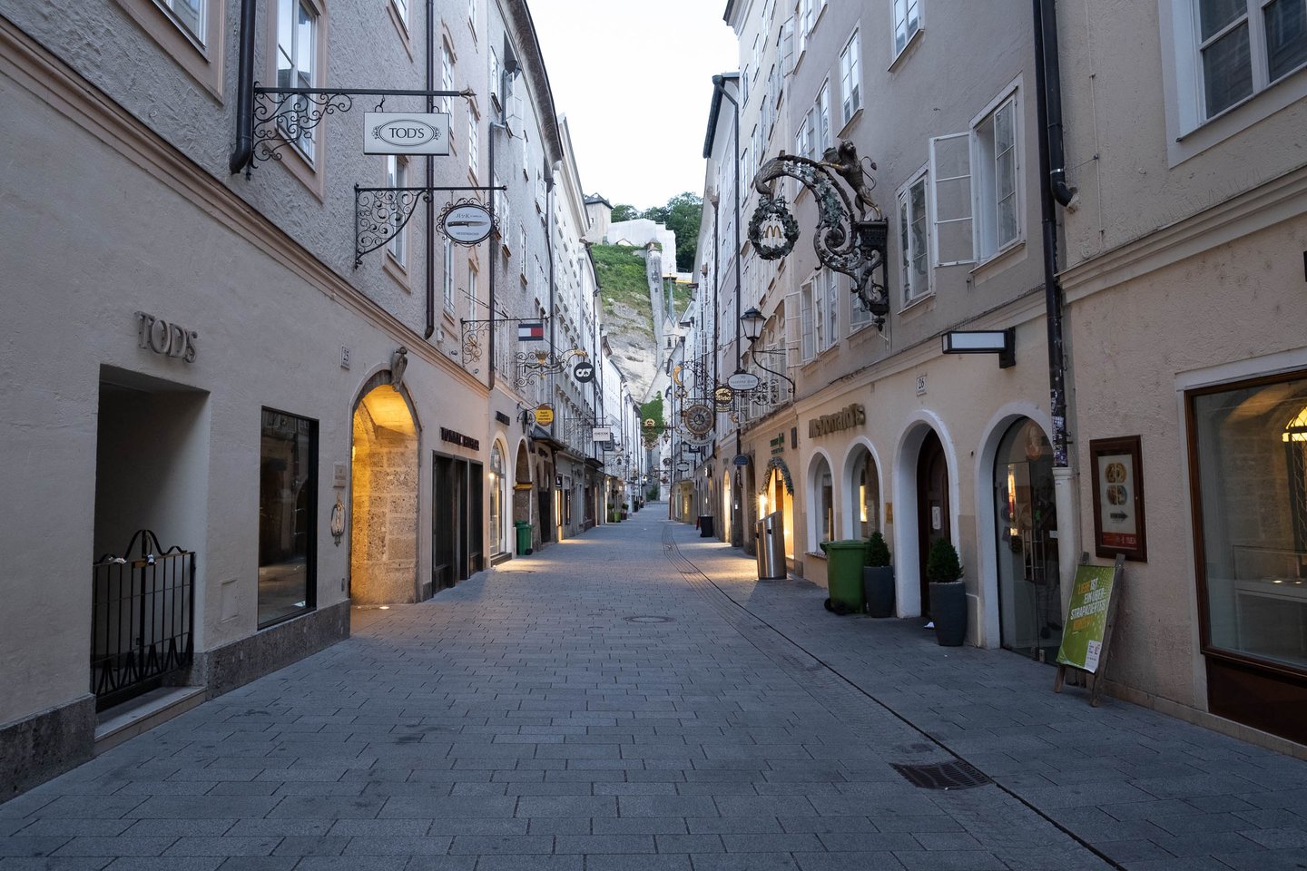 Quiet narrow shopping alley Goldgasse at early morning with TODs and other shop signs above closed shutters in Salzburg Altstadt