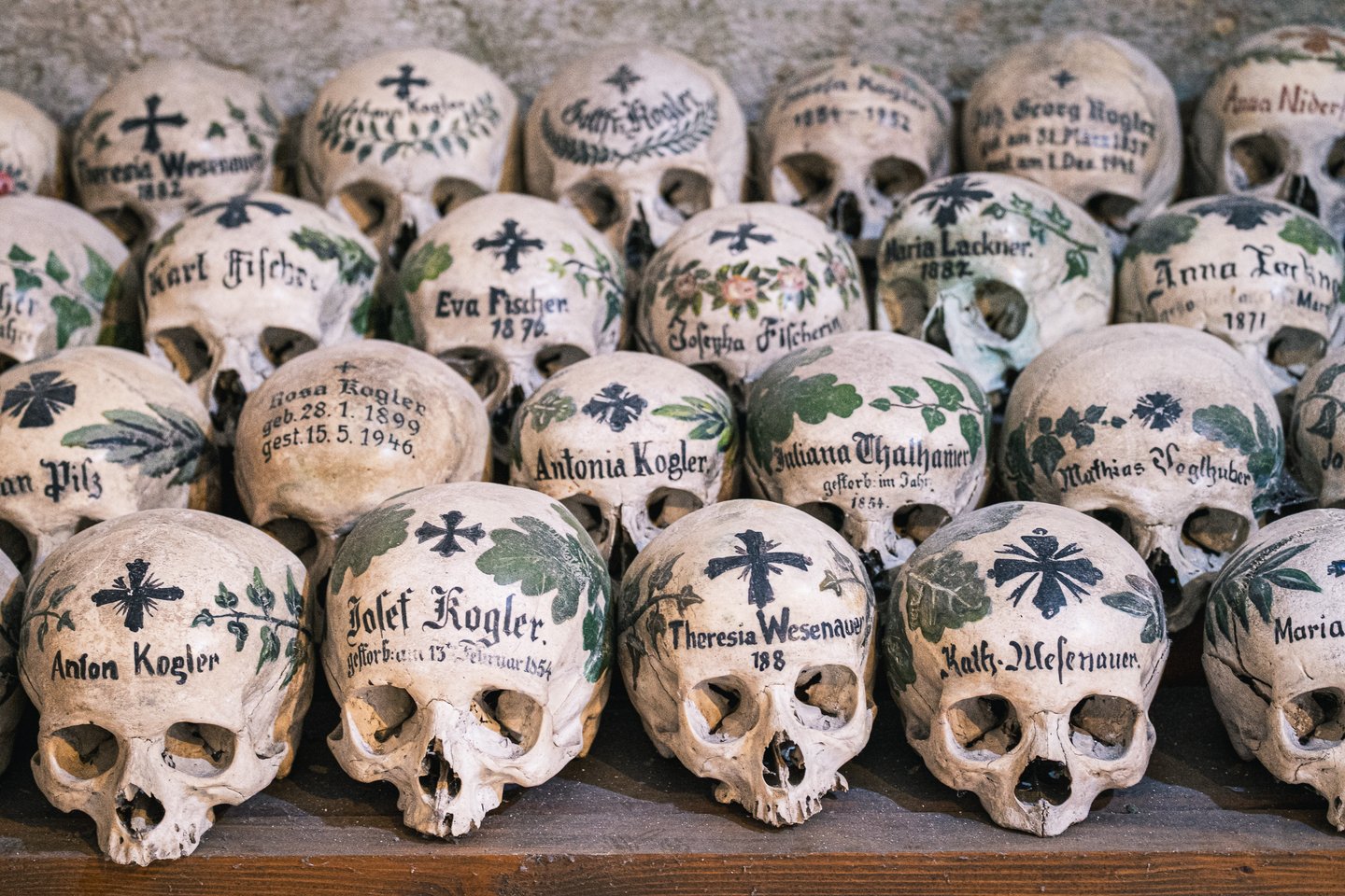 Rows of skulls painted with names, dates, crosses and leafy wreaths stacked on a wooden shelf in the Hallstatt bone house.