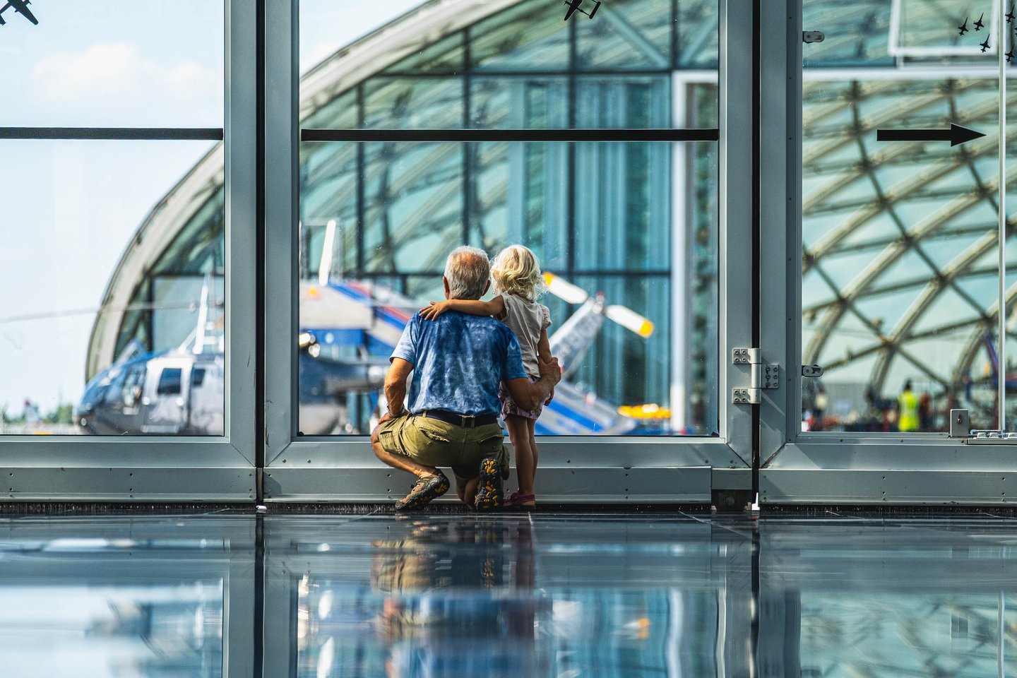 A man and small child crouch at the glass wall watching aircraft inside Hangar-7 in Salzburg.