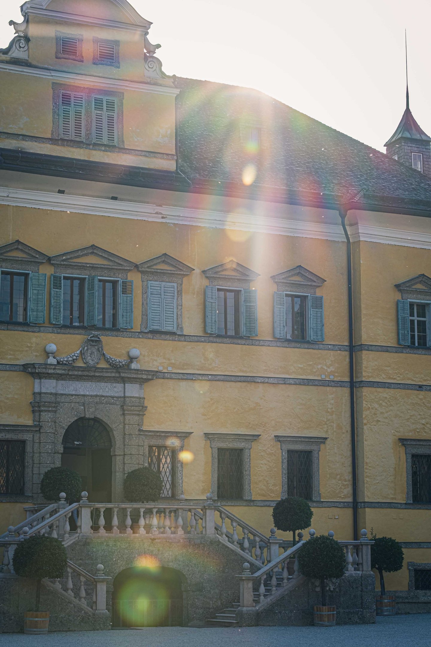 Yellow Hellbrunn Palace facade with grand staircase and sun flare overhead in Salzburg.