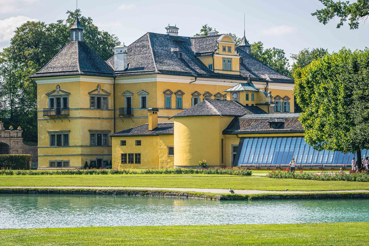 Yellow Baroque Hellbrunn Palace reflected in pond with summer greenery in Salzburg.