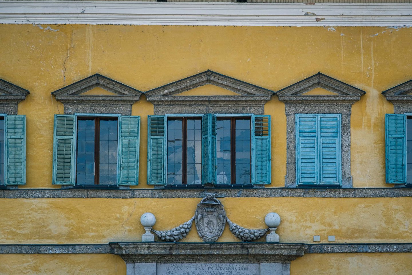 Row of pedimented windows with turquoise shutters on the yellow Hellbrunn Palace facade in Salzburg.