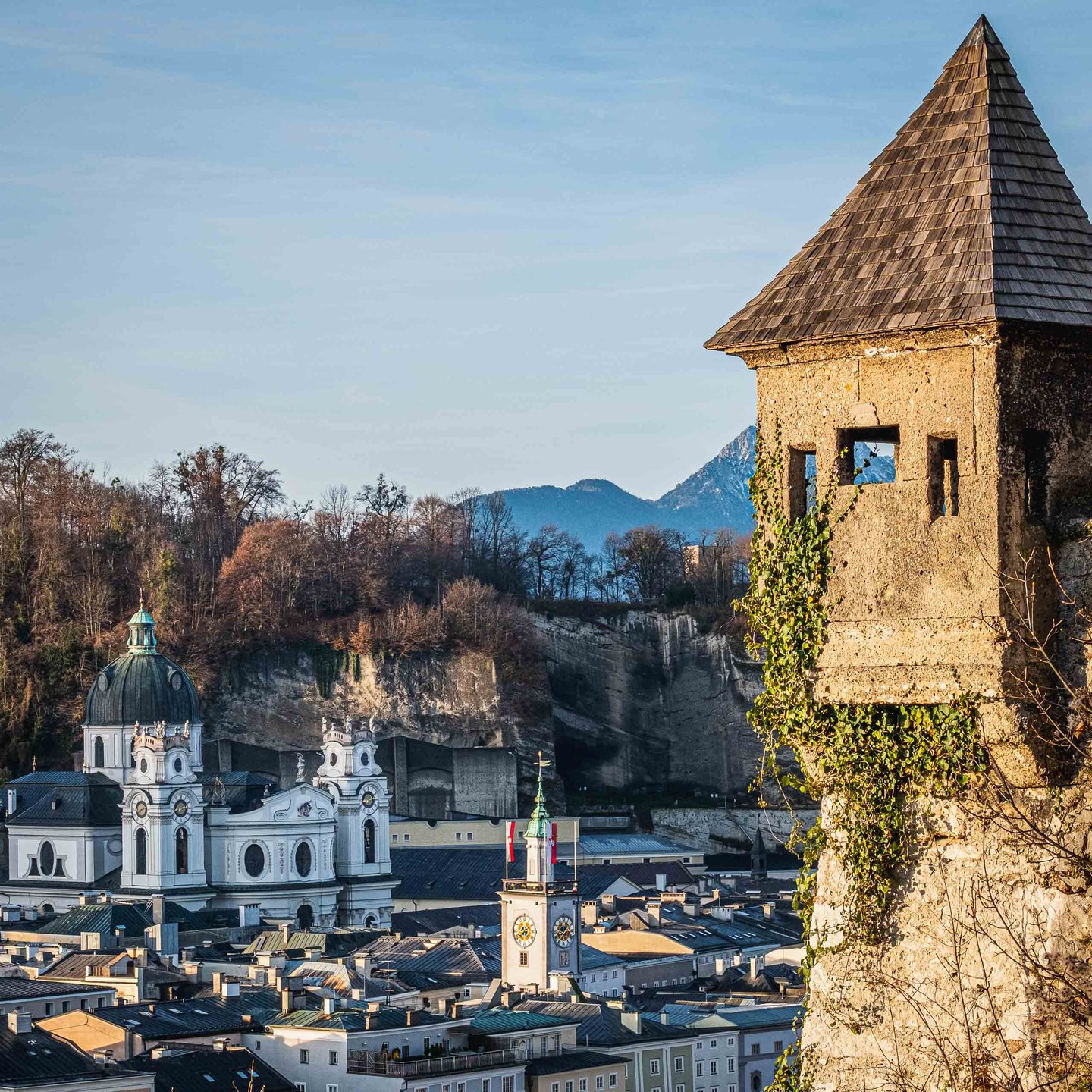 Ivy-covered tower of Hettwer Bastei frames Kollegienkirche and Altes Rathaus clock tower in Salzburg old town.