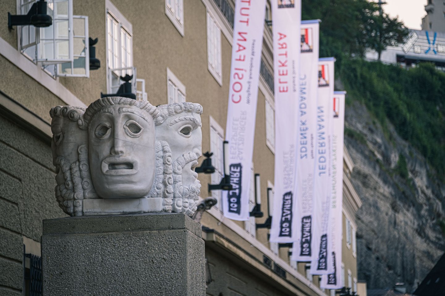 Theatrical mask sculpture with Salzburg Festival Jedermann and Elektra banners at Hofstallgasse.