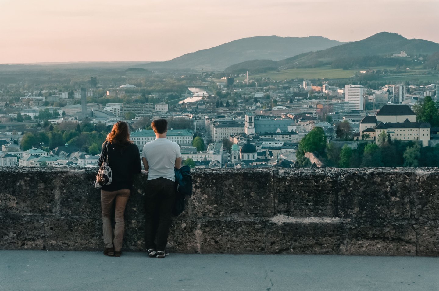 Couple looks out over the Salzburg skyline at dusk from a Hohensalzburg fortress terrace in Salzburg
