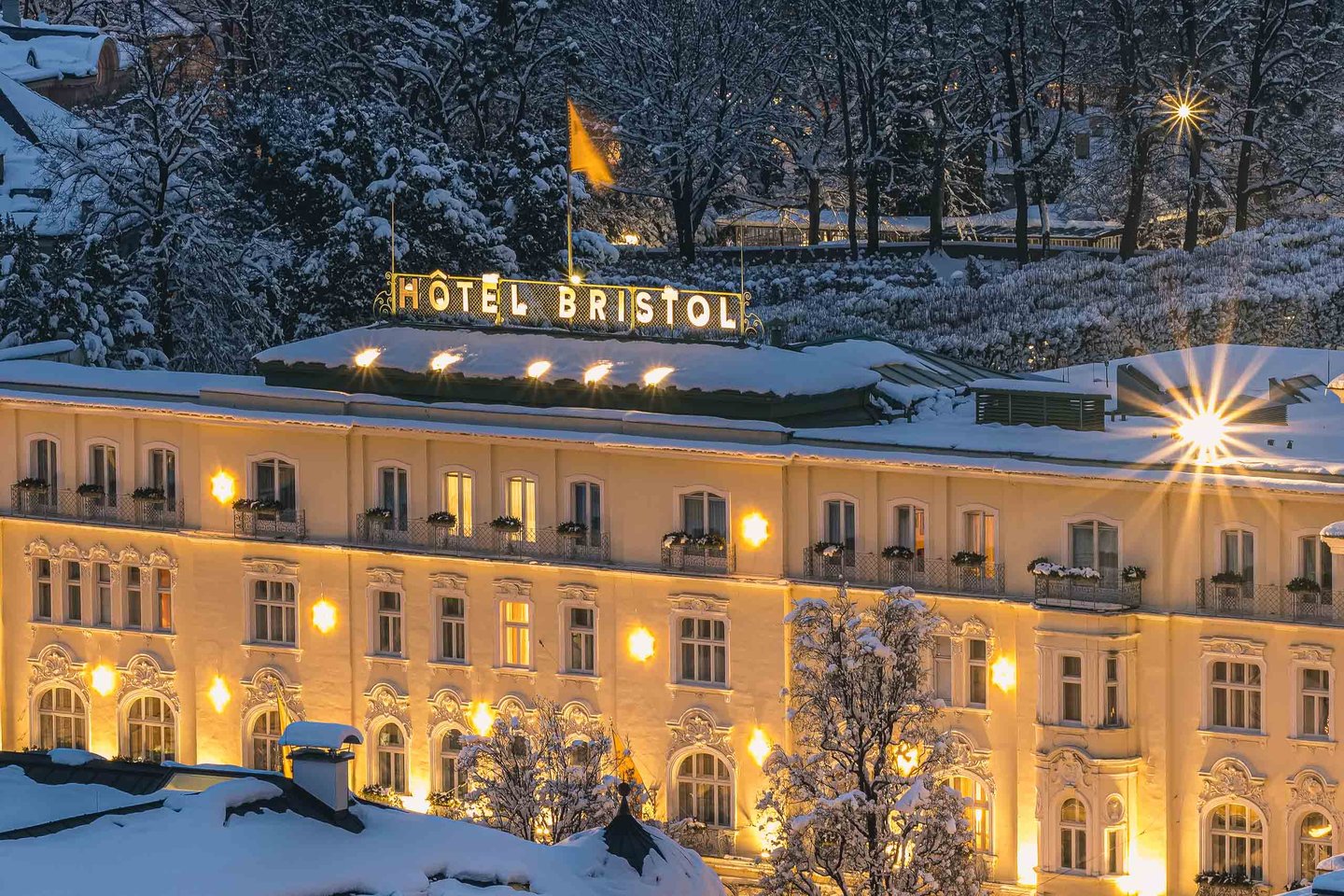 Hotel Bristol Salzburg facade lit at night with snow-covered roofs and trees in Salzburg