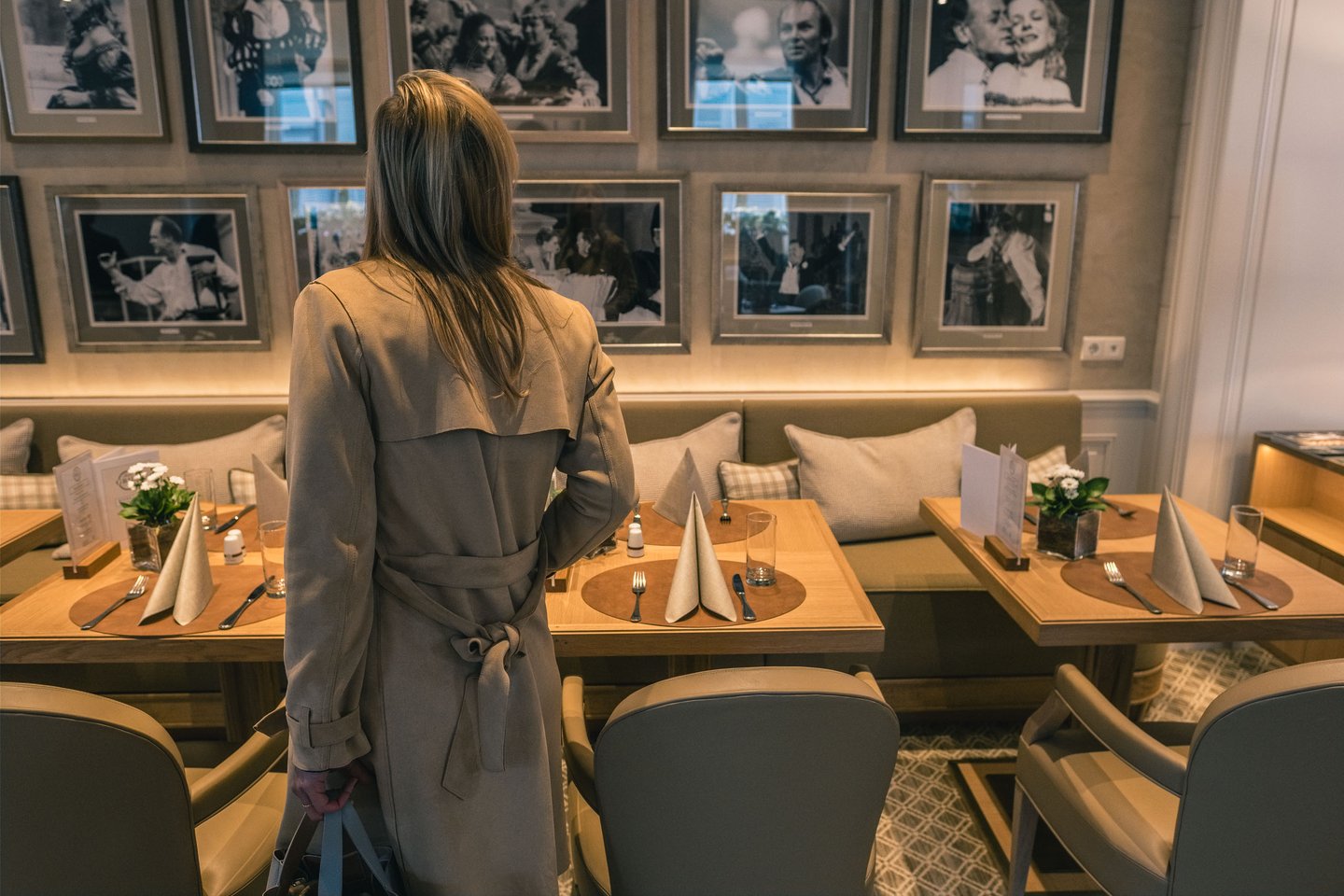 Guest in trench coat standing by tables in Hotel Sacher Salzburg dining room with portrait wall