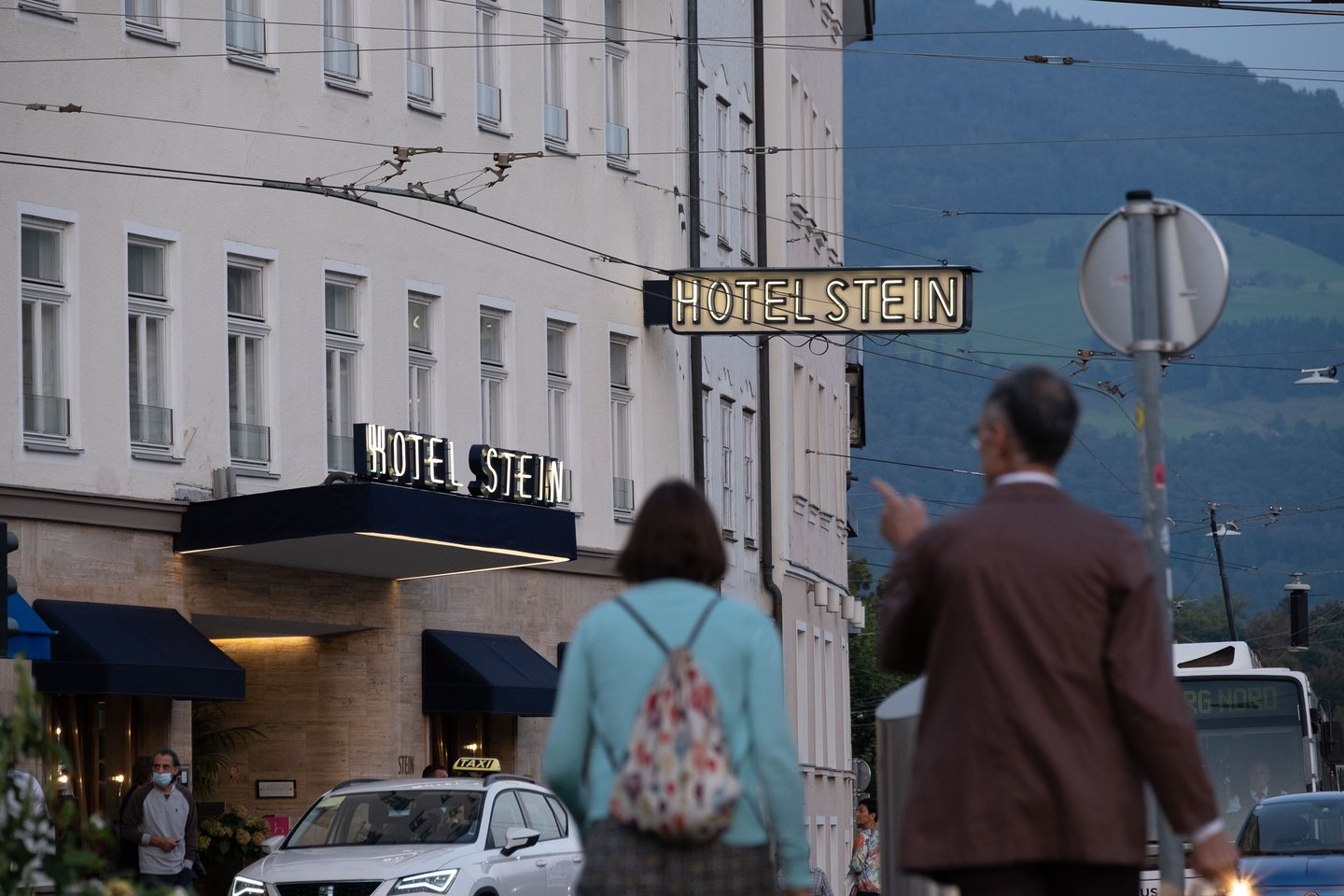 Illuminated Hotel Stein sign at the entrance with passersby on Giselakai in Salzburg