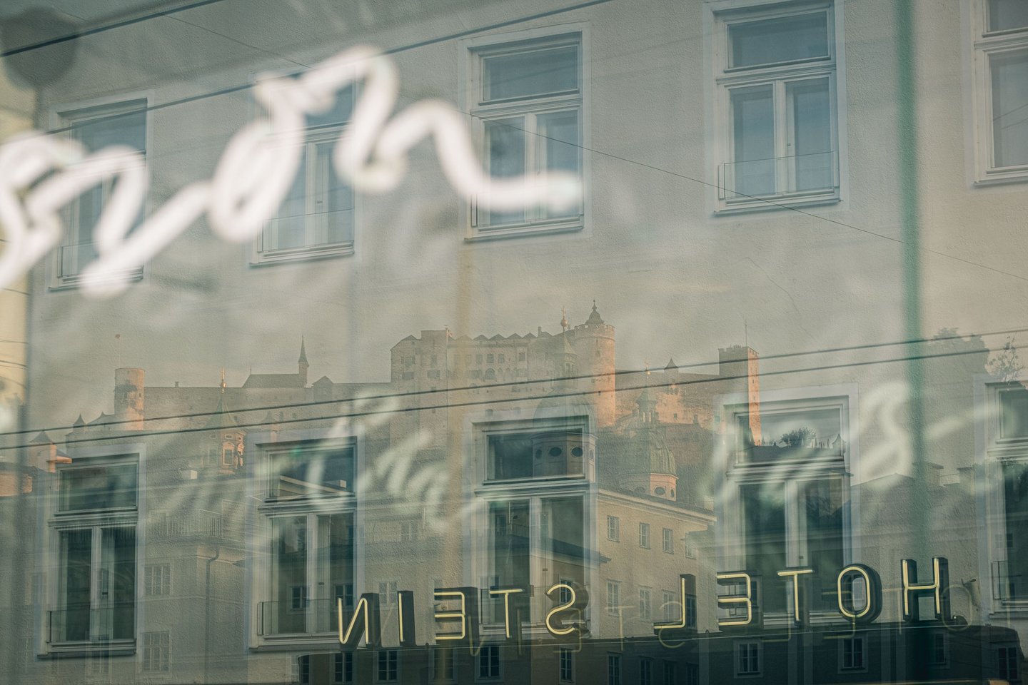 Hohensalzburg Fortress reflects in the Hotel Stein window above Hotel Stein lettering in Salzburg
