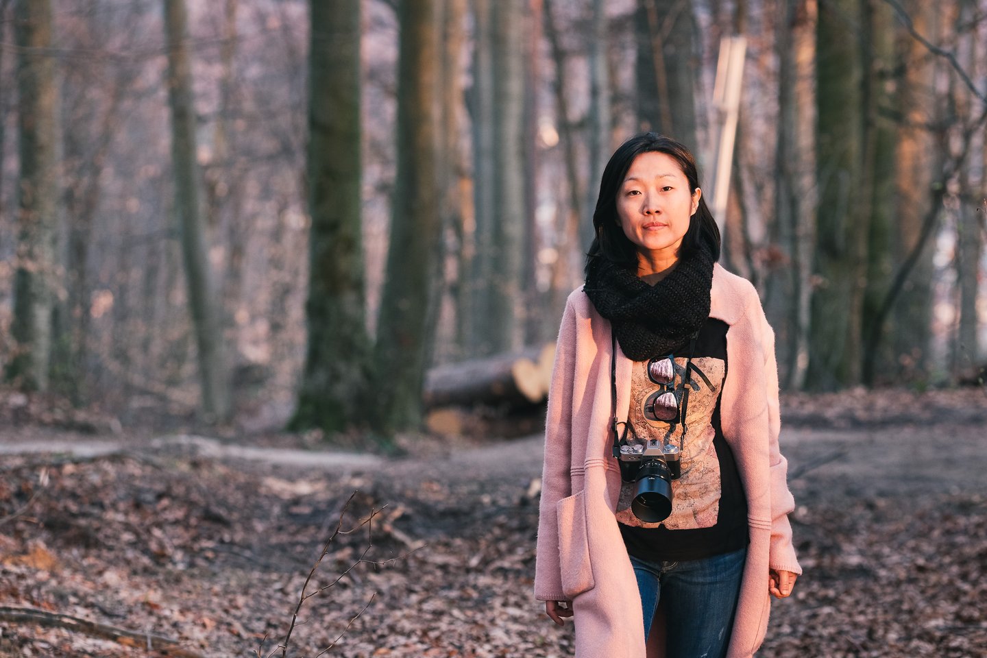 Hyunok Jang stands in a leafless beech forest on the Kapuzinerberg in Salzburg with a camera around her neck in low evening light.