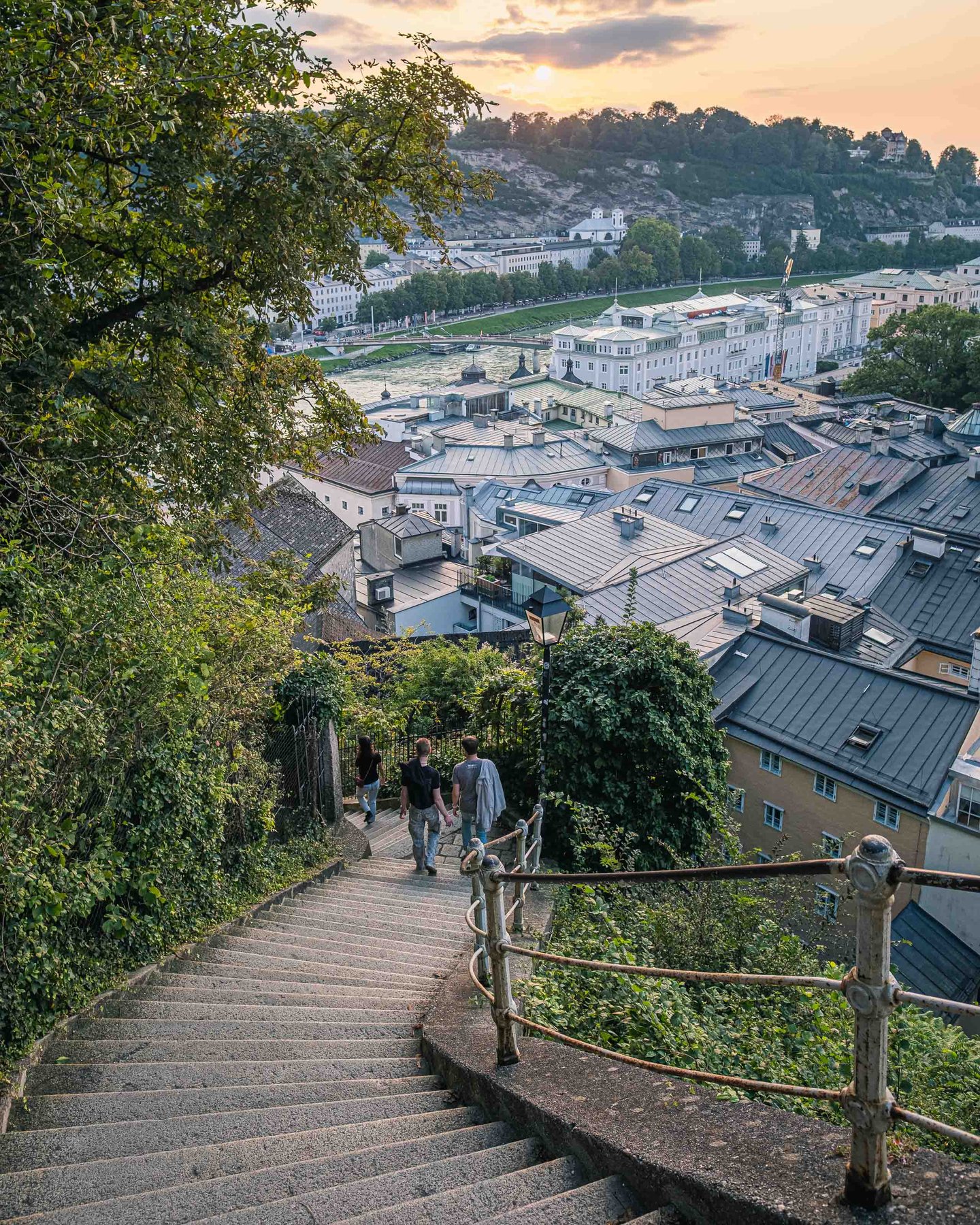 Walkers descend the Imbergstiege steps toward Altstadt rooftops at sunset in Salzburg