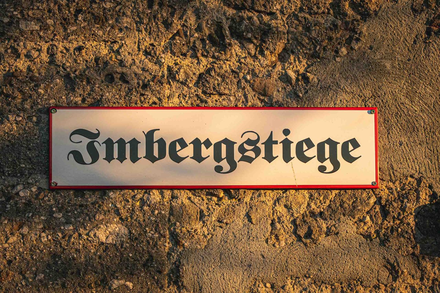 Enamel street sign reading Imbergstiege in blackletter font mounted on rough stone in Salzburg.