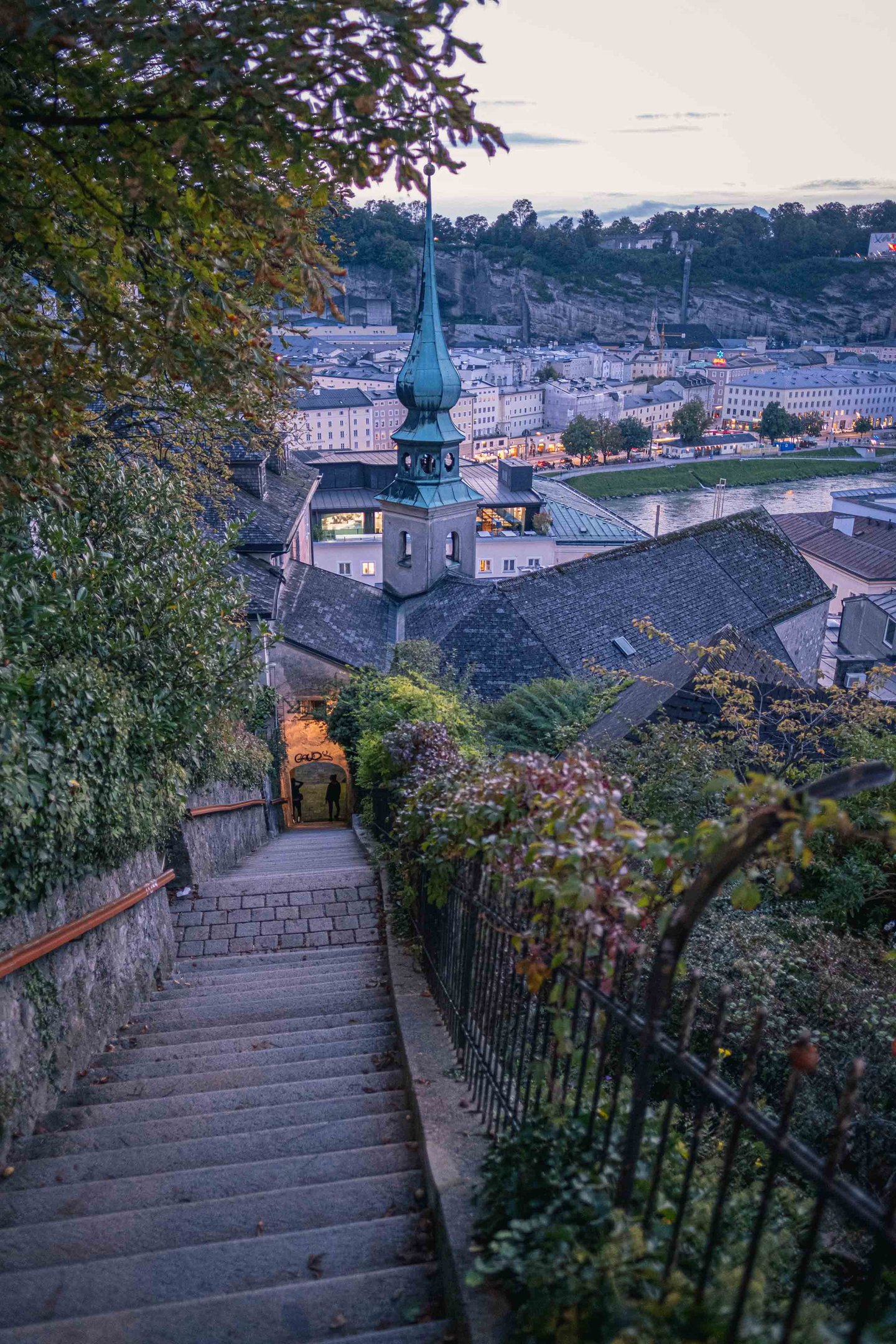 Imbergstiege stairway descending toward the Salzach with tower and Altstadt rooftops at dusk in Salzburg