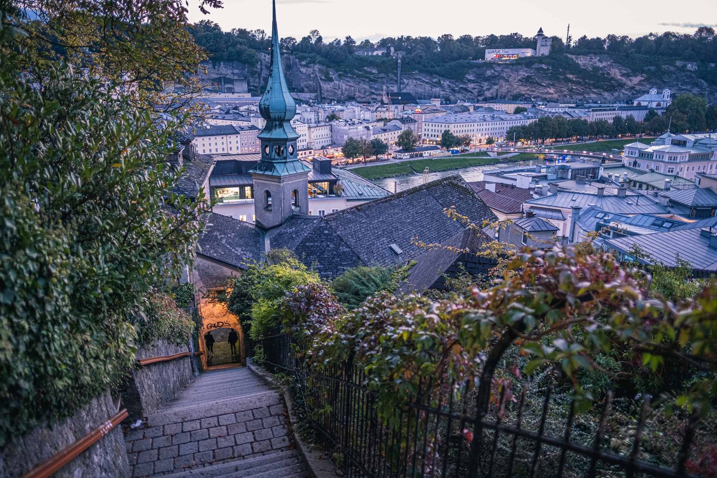 Imbergstiege stairway descending with a spire silhouetted above Altstadt rooftops at twilight in Salzburg