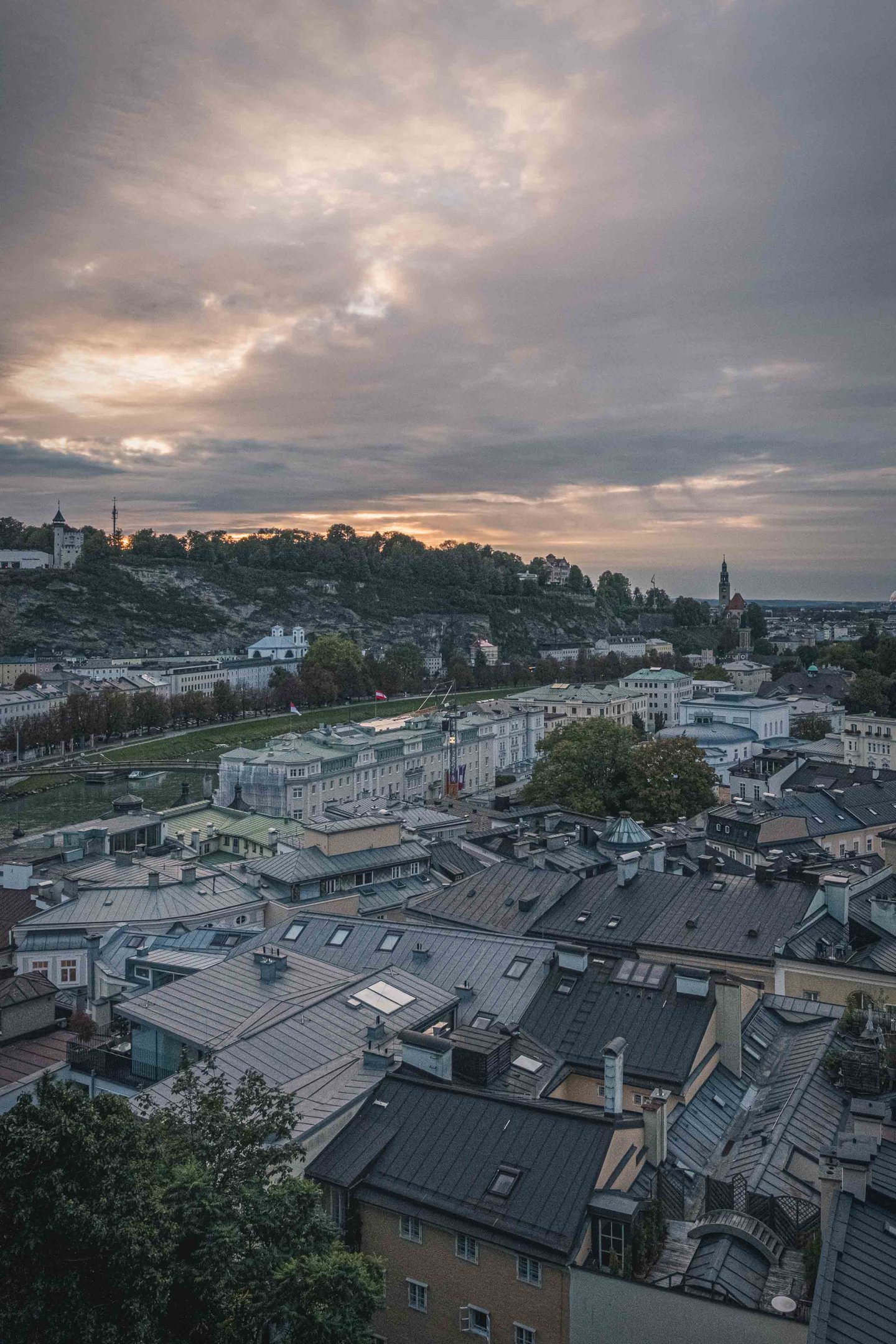 Rooftops of Salzburg Neustadt with Mönchsberg hill and Richterhöhe tower under cloudy sunset sky