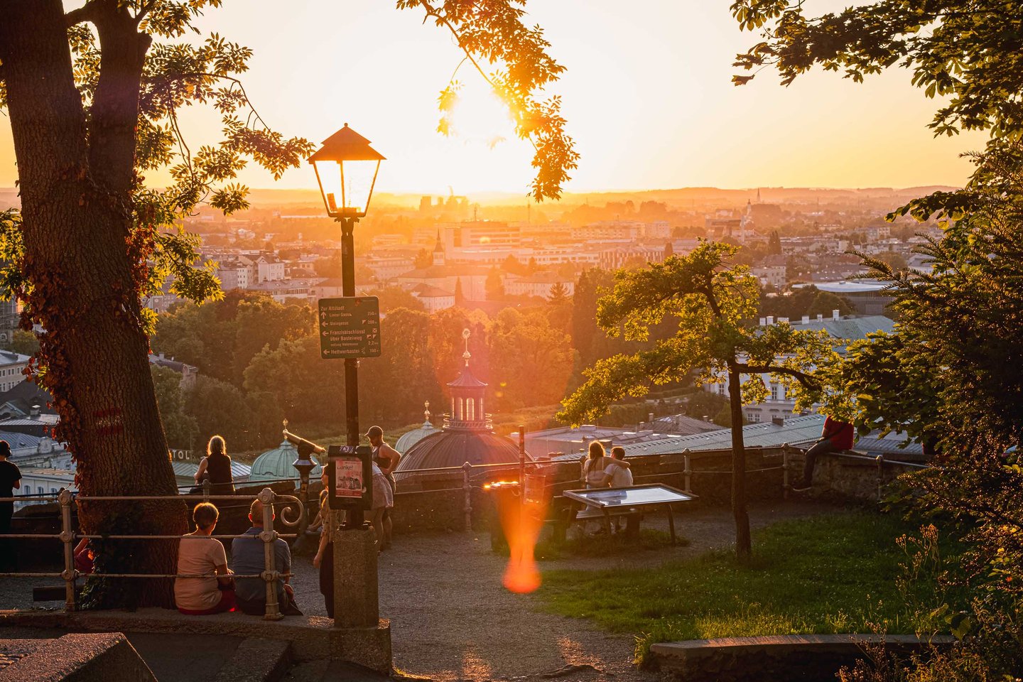 Visitors gathered at Kapuzinerberg summit viewpoint watching the sunset over Salzburg city.