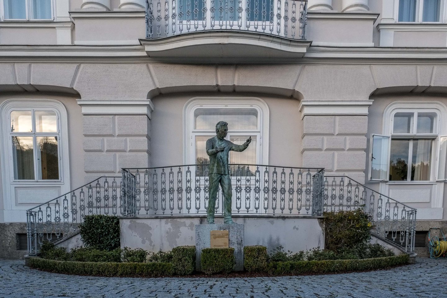 Bronze statue of a conducting figure in front of ornate balcony and windows of a villa in Salzburg.