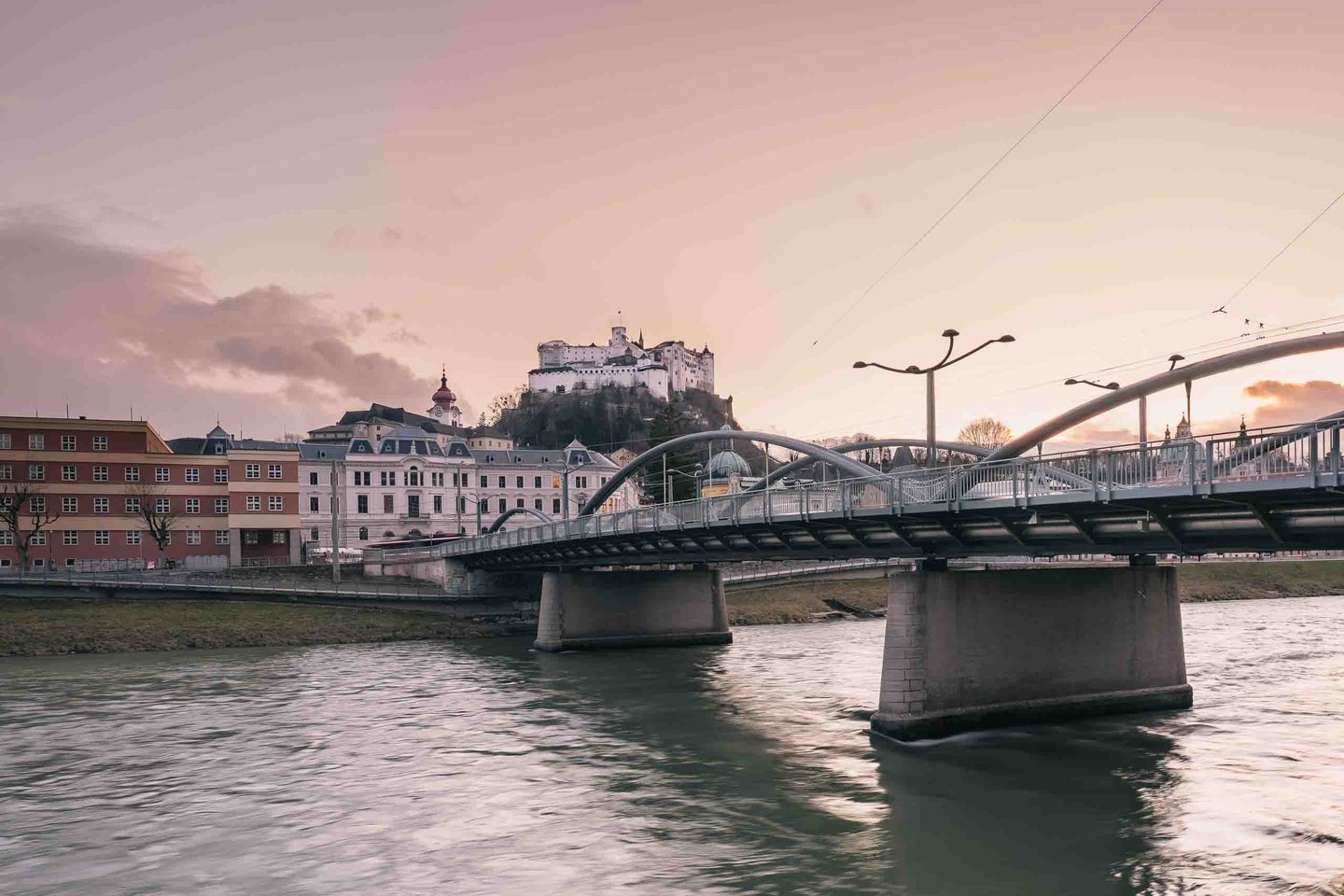 Metal-arch Karolinenbruecke over the Salzach at sunset with Hohensalzburg Fortress rising above the Altstadt in Salzburg