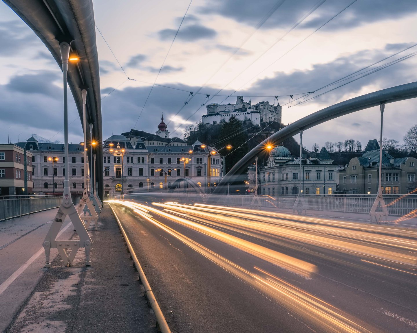 Long-exposure light trails of traffic on the Karolinenbruecke at dusk with Hohensalzburg Fortress on the hill