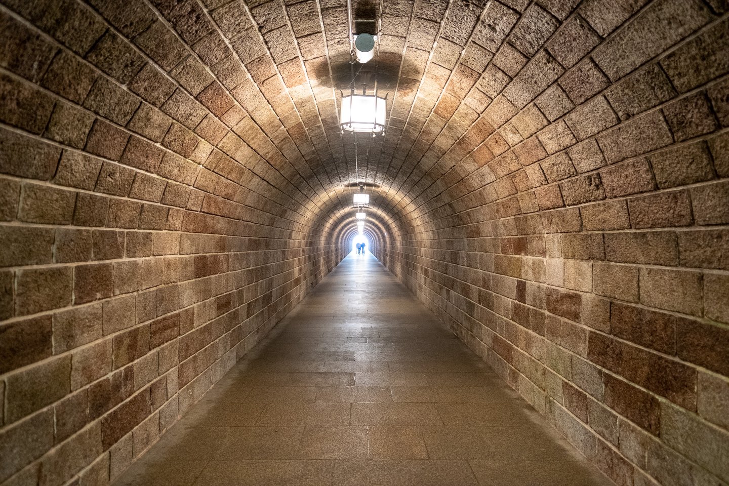 The long vaulted stone tunnel that runs from the Kehlstein bus stop to the Eagle's Nest lift, two small figures silhouetted at the bright far end.