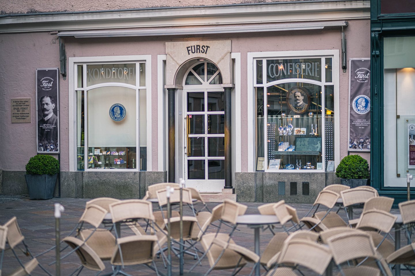 Konditorei Fürst storefront with empty cafe chairs outside on Alter Markt in Salzburg old town.